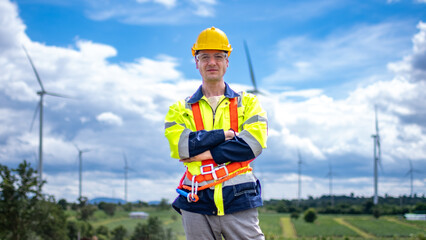 Engineer or architect with helmet posing on construction site with infrastructures of wind turbine farm with blue sky background. Foreman working in renewable energy business.