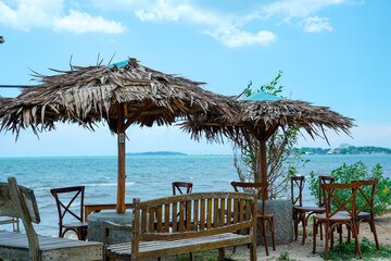 view of the seating area with large straw umbrellas with a backdrop of a beachfront view with bright blue skies and a horizon that reveals land in the distance.