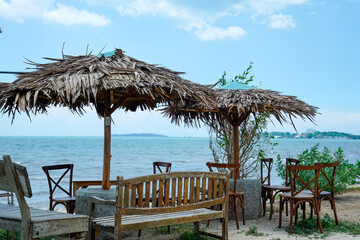 view of the seating area with large straw umbrellas with a backdrop of a beachfront view with bright blue skies and a horizon that reveals land in the distance.