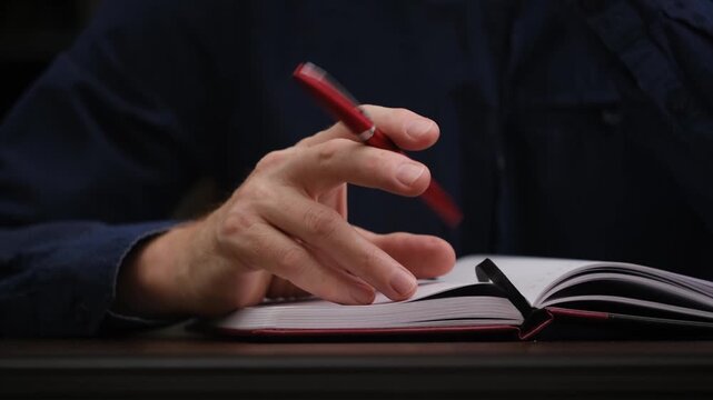 unfocused man sitting at desk during meeting or class, nervously spinning red pen between his fingers out boredom, showcasing common sign procrastination or anxiety. close up.
