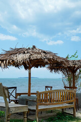 view of the seating area with large straw umbrellas with a backdrop of a beachfront view with bright blue skies and a horizon that reveals land in the distance.