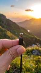 Hand holds small digital cable connector against a sunrise mountain backdrop