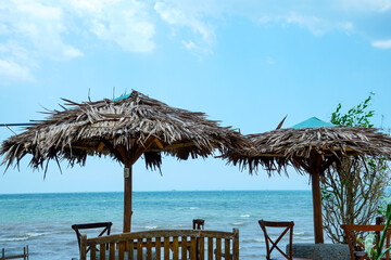 view of the seating area with large straw umbrellas with a backdrop of a beachfront view with bright blue skies and a horizon that reveals land in the distance.