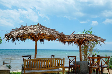 view of the seating area with large straw umbrellas with a backdrop of a beachfront view with bright blue skies and a horizon that reveals land in the distance.