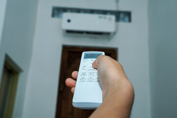 view of a hand holding the AC remote control with the AC mounted on the wall.