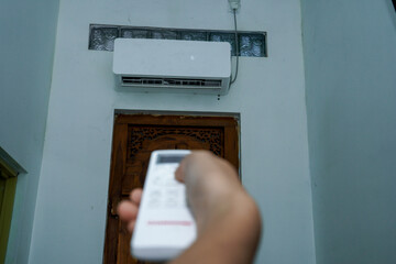 view of a hand holding the AC remote control with the AC mounted on the wall.