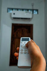 view of a hand holding the AC remote control with the AC mounted on the wall.
