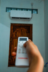 view of a hand holding the AC remote control with the AC mounted on the wall.