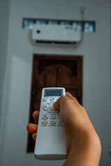 view of a hand holding the AC remote control with the AC mounted on the wall.