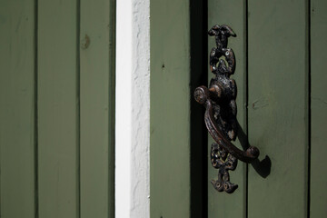 An ornate, dark metal door handle adorns a weathered green wooden door, highlighted by a stark white frame.