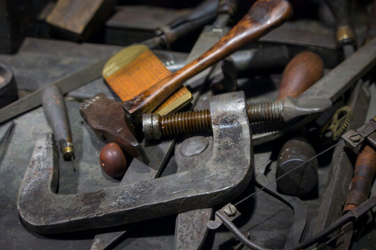 A close-up shot reveals a collection of vintage metal hand tools, including a prominent C-clamp and various other implements, resting on a workbench.