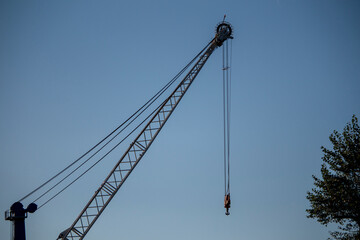 Naklejka premium The lattice boom and hook block of a large industrial crane are silhouetted against a clear blue sky on a sunny day.