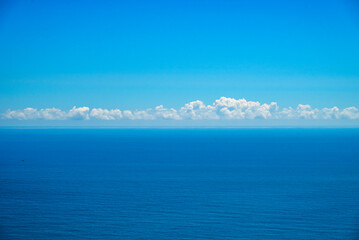 A calm ocean under a clear blue sky, with some fluffy clouds chilling on the horizon.