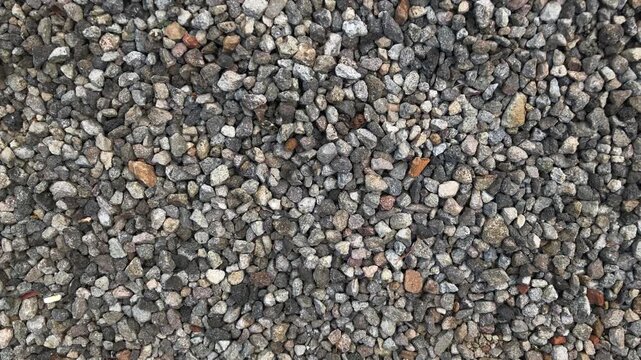 Top view texture of small rocks, showing irregular stones in shades of gray, brown, and beige with rough natural patterns. pebbles. High angle, above. background.