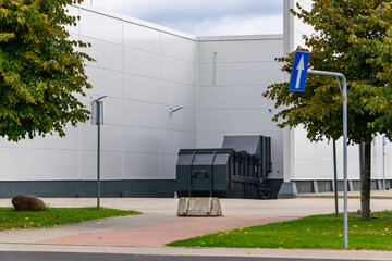 Waste container next to back wall of building, concrete barrier and traffic sign, facility service area, garbage storage point, industrial surroundings