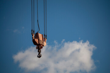 Fototapeta premium A heavy-duty crane hook and block assembly are suspended against a bright blue sky with scattered clouds.