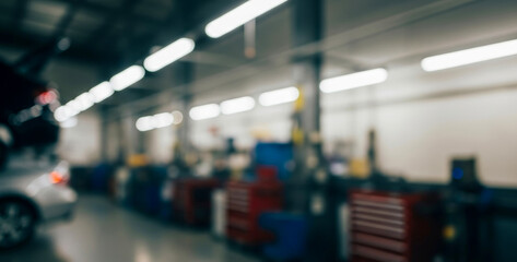 Blurry interior of a vehicle repair shop with bright overhead lights highlighting silhouettes of tools, machinery, and working stations inside a spacious modern industrial environment