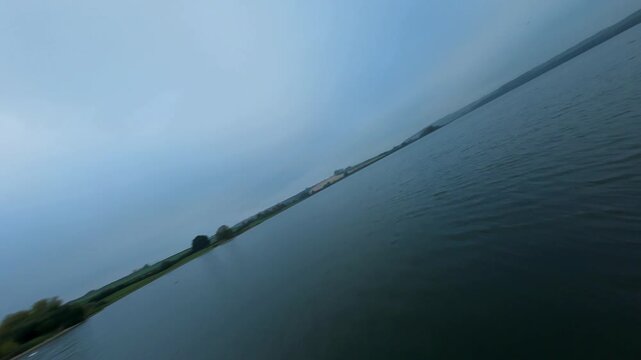 FPV drone aerial view close flying over wetland reserve with wild waterfowl birds and water control structures on reservoir late evening blue hour cloudy autumn night, United Kingdom 