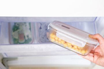 A female hand holds a glass box with chickpeas against the background of drawer in the freezer, top view.