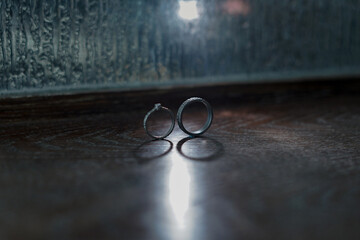 two silhouettes of silver wedding rings illuminated by dim light on a wooden table