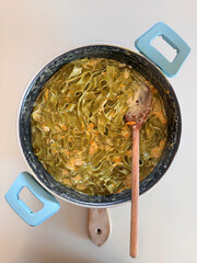 directly above shot of spinach fettucine pasta with cream sauce in pot on table with wooden spoon