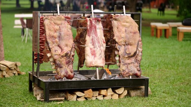 Wide shot of Argentine asado with beef ribs and sausages roasting slowly over wood fire outdoors.