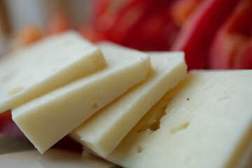 Slices of cheese next to fresh red vegetables on the table