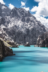 Vertical view of the bright turquoise Kol Suu Lake water surrounded by towering, sheer, grey-toned mountain and canyon walls