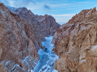Aerial view looking down the narrow, towering canyon walls of Kel Suu Lake with a partially frozen river of ice below