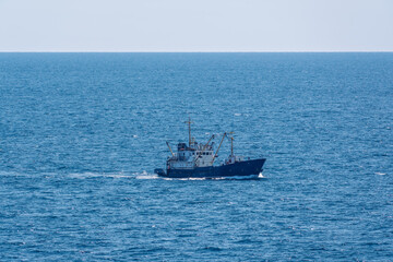 Fishing boat in blue sea and clear sky with birds flying overhead.
