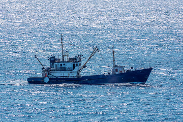 Fishing boat in blue sea and clear sky with birds flying overhead.