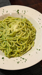 Spaghetti al Pesto in a dish over a white plate and wooden table	
