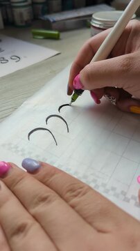 Ink pen writing session, artist shaping artistic letters on paper. Concept of creativity, craftsmanship, and traditional calligraphy skills. Female hand of artist.