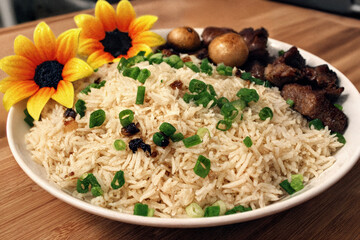 A beautifully presented rice dish garnished with fresh green onions, accompanied by savory meat and mushrooms, adorned with bright yellow flowers for an appealing and vibrant touch
