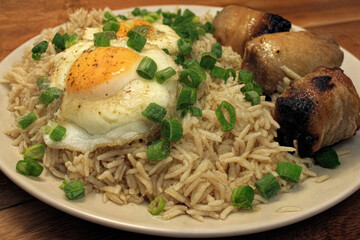 A hearty dish featuring flavorful rice topped with sunny-side-up eggs and paired with savory grilled pork, garnished with fresh green onions.