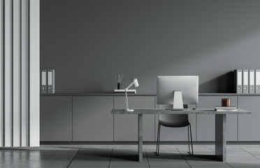 Fototapeta premium Modern minimalist office with grey walls, desk, and furniture, featuring desktop computer, folders, and lamp in a sleek workspace. 3D Rendering