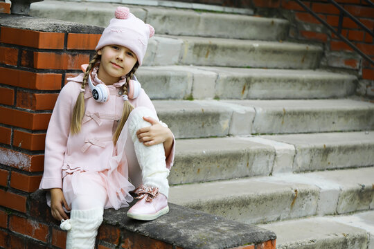 Cute Girl in Pink Outfit with Headphones Relaxing on Steps Outdoors