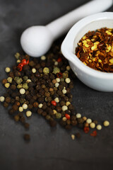 Assorted Peppercorns and Chili Flakes in White Ceramic Bowl with Pestle on Dark Background