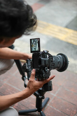 Person operating a professional video camera on a gimbal outdoors, focusing on the screen to capture footage.