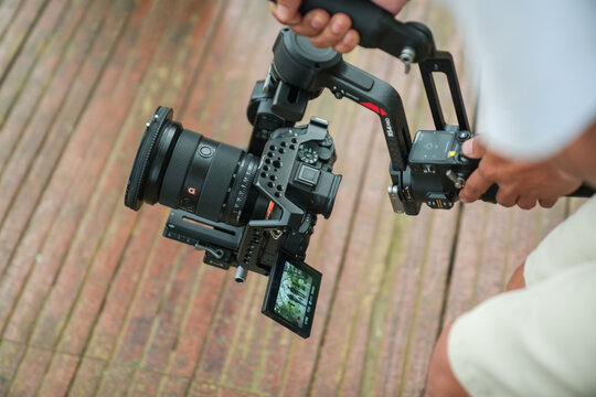 A filmmaker operates a professional mirrorless camera mounted on a handheld gimbal stabilizer for smooth video recording.