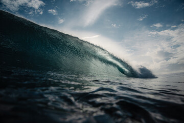 Fototapeta premium A powerful ocean wave curls into a barrel as it breaks under a dramatic, sunlit sky.