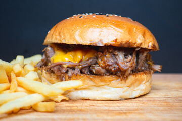 Pulled pork burger with cheese and french fries on wooden board.