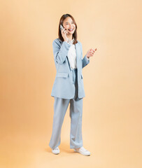 Confident Asian businesswoman talking on mobile phone and smiling on beige color background.
