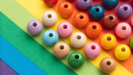 Scattered wooden-textured beads on rainbow paper background, displaying natural grain patterns in pink, orange, yellow, green, blue, purple, and cream tones.