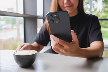 Closeup image of a woman holding and using mobile phone while drinking coffee in cafe