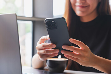 Closeup image of a woman using smart phone and laptop computer in cafe