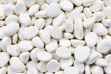 A dense, irregular pile of smooth white pebbles on a bright, minimalist white background. A top down perspective of a dense, irregular pile of smooth, polished white pebbles. The pebbles vary slightly