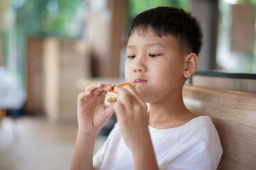 young boy is eating a sandwich, Asian boy is happily eating food.