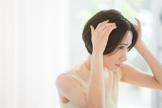 黒髪ボブヘアのミドル世代の日本人女性が髪を触っている。