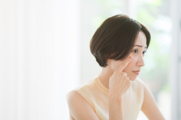 鏡を見ながら顔を触るミドル世代の日本人女性。